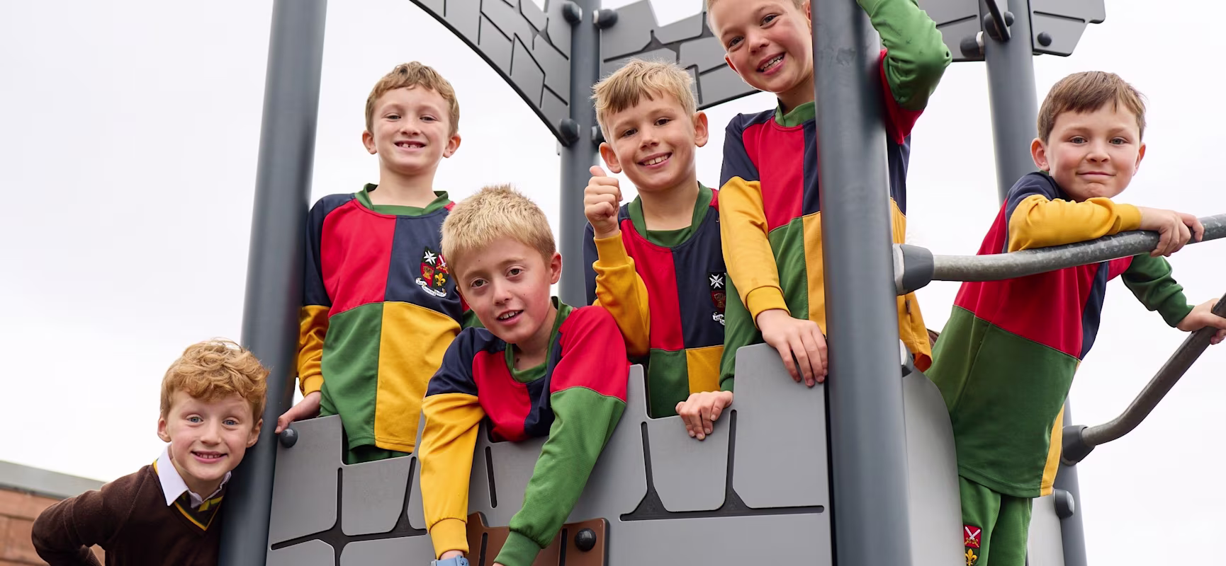 Group of children in colourful school sports kits playing on a tall grey castle-themed playground structure outdoors