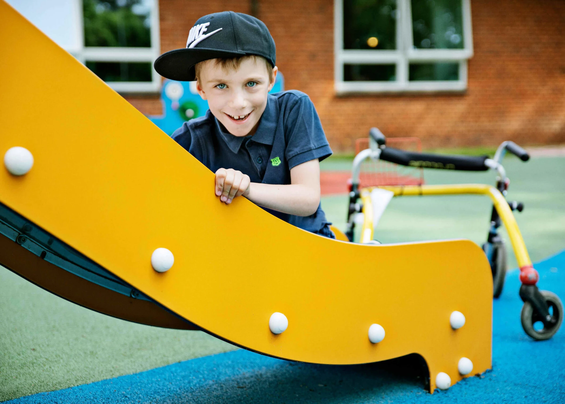 Boy with a walker sitting on a slide on inclusive play system