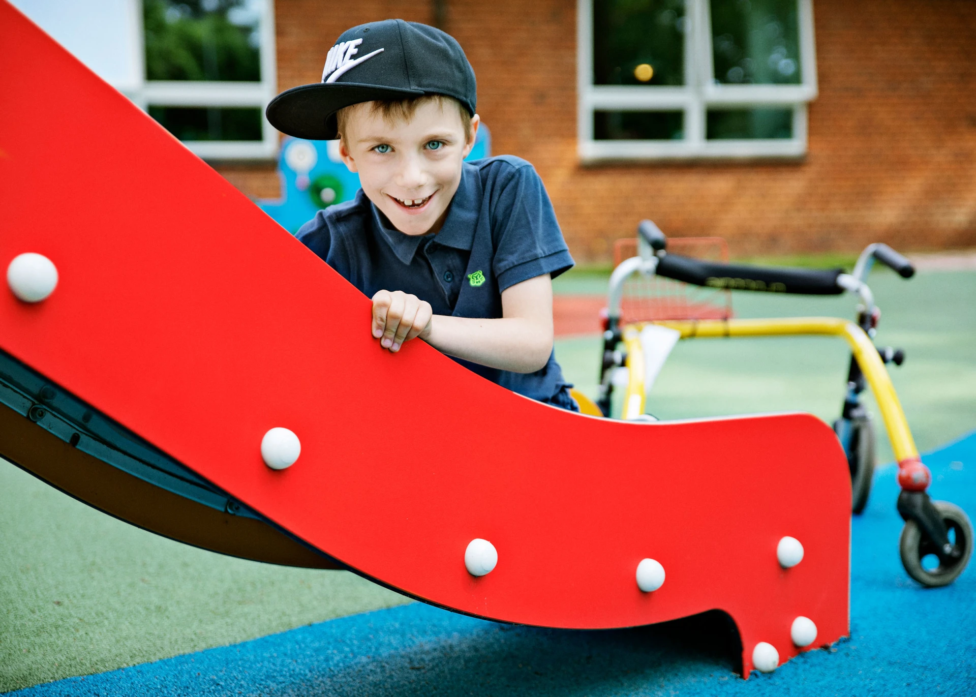 Boy with a walker sitting on a slide on inclusive play system