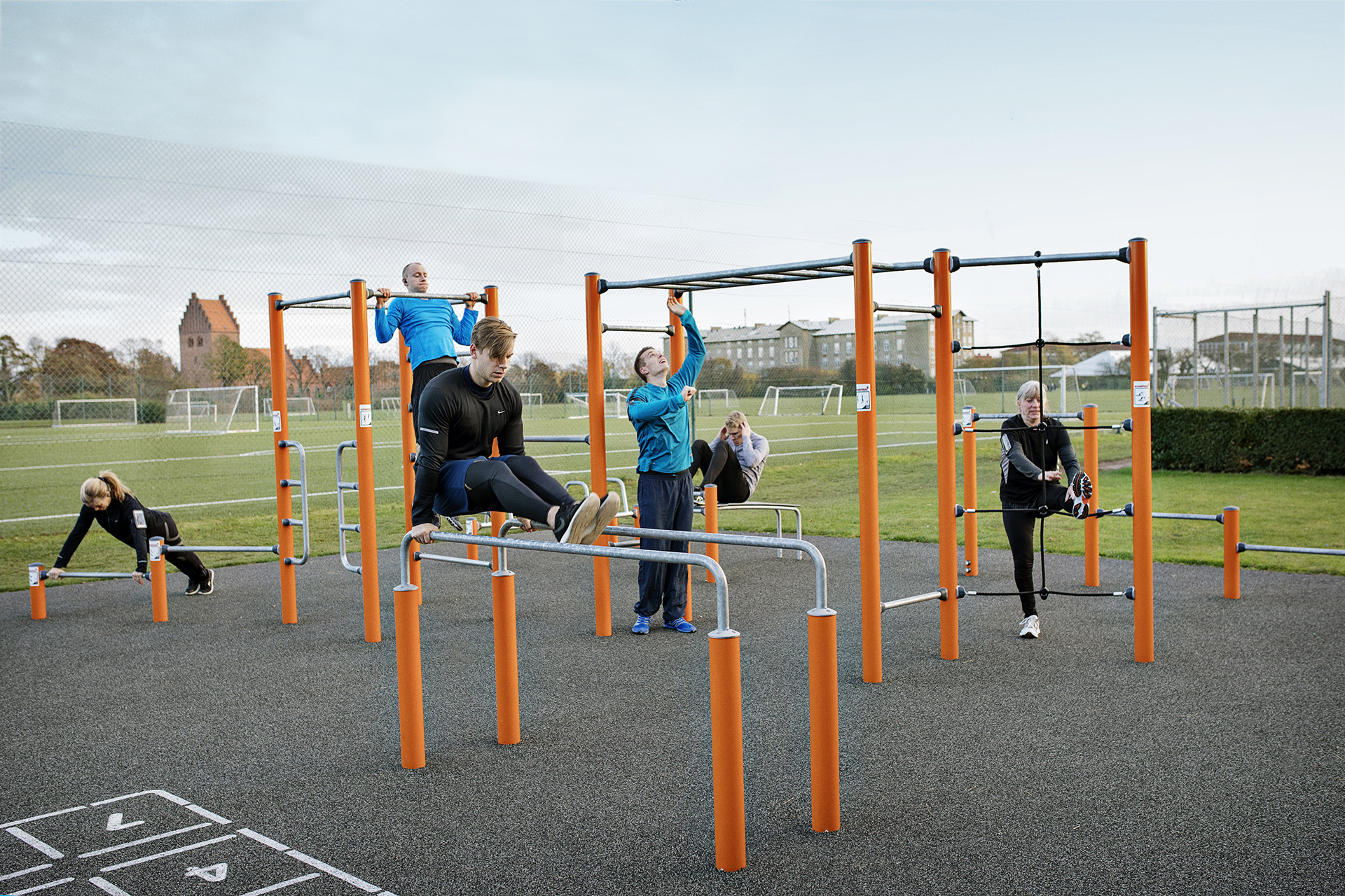 Women exercise on green outdoor gym equipment, one doing incline push-ups while others use horizontal bars in the background.