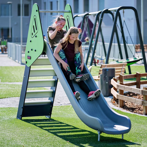 girls sliding down a playground slide on a school playground