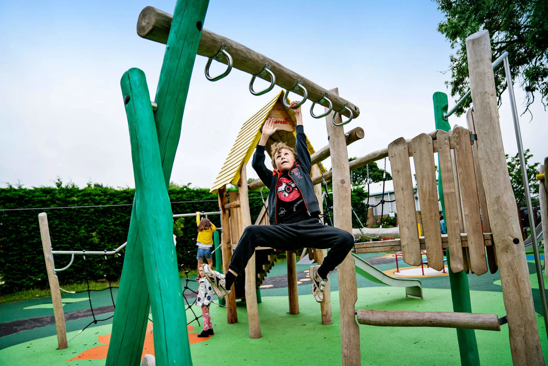 Boy swings from hand to hand on wooden playstructure in Poppleton