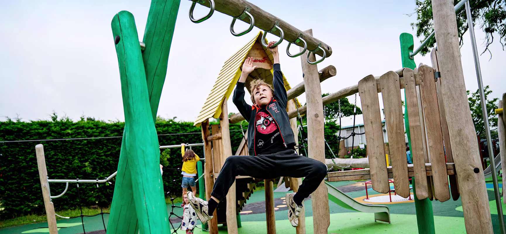 Boy swings from hand to hand on wooden playstructure in Poppleton