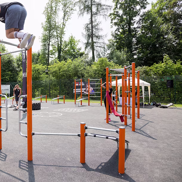 Mann klettert an einer Hinderniswand mit Kletternetz auf einem Hindernisparcours im Freien