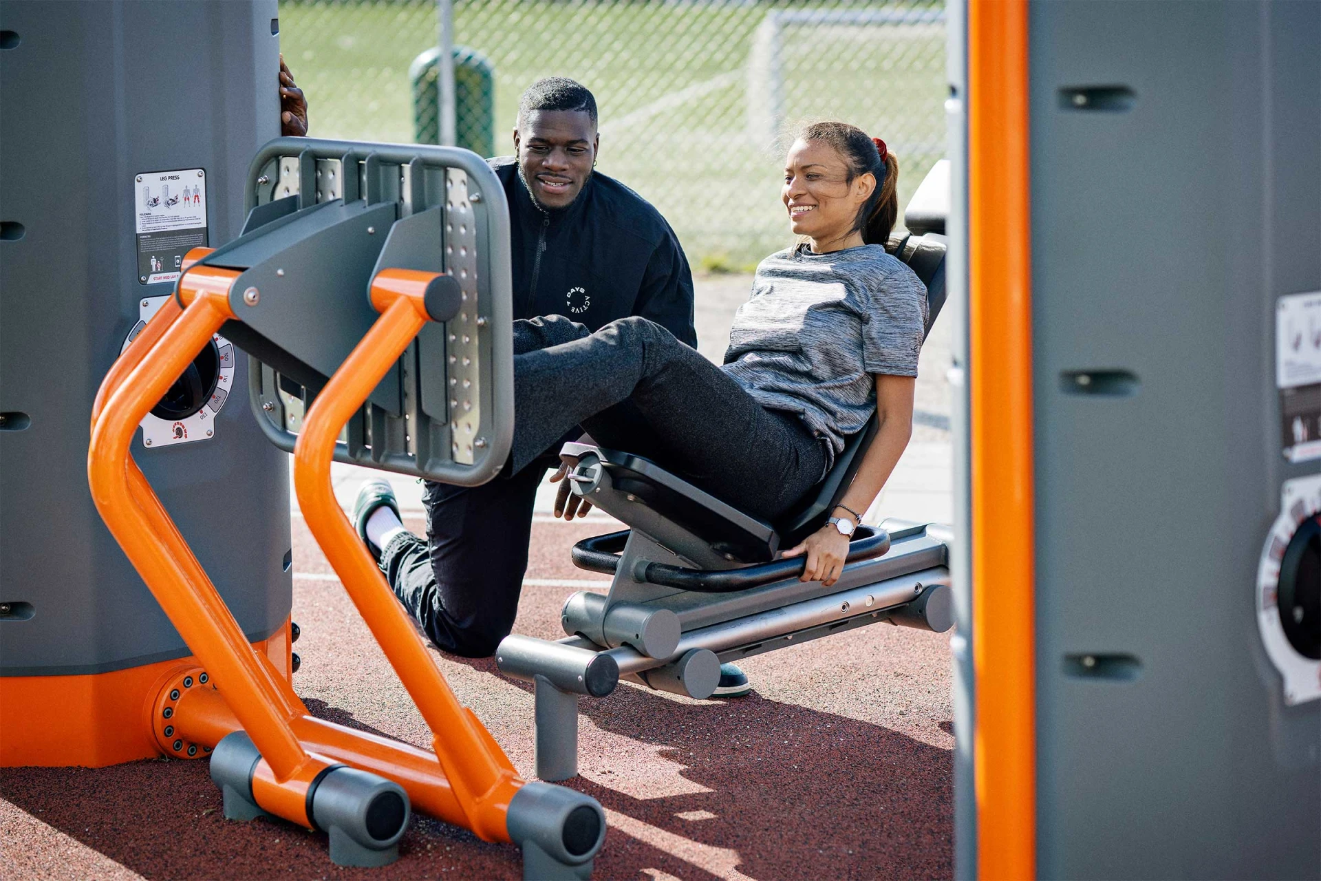A woman working with a personal training on an outdoor leg press from KOMPAN
