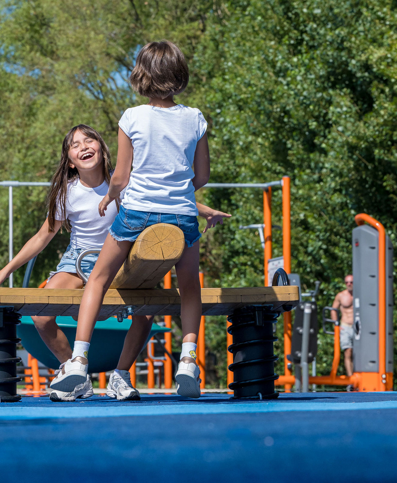 children having fun on a seesaw while adults working out in the background.