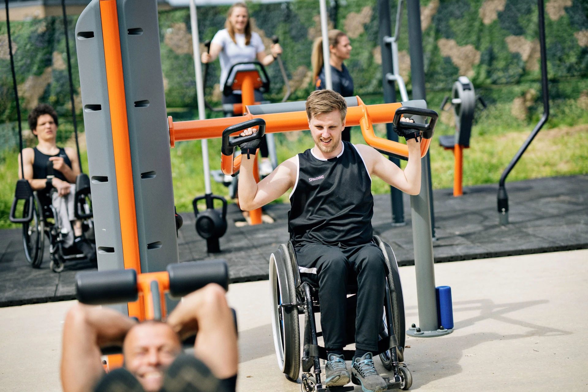 A man in a wheelchair working out on an outdoor overhead shoulder press machine
