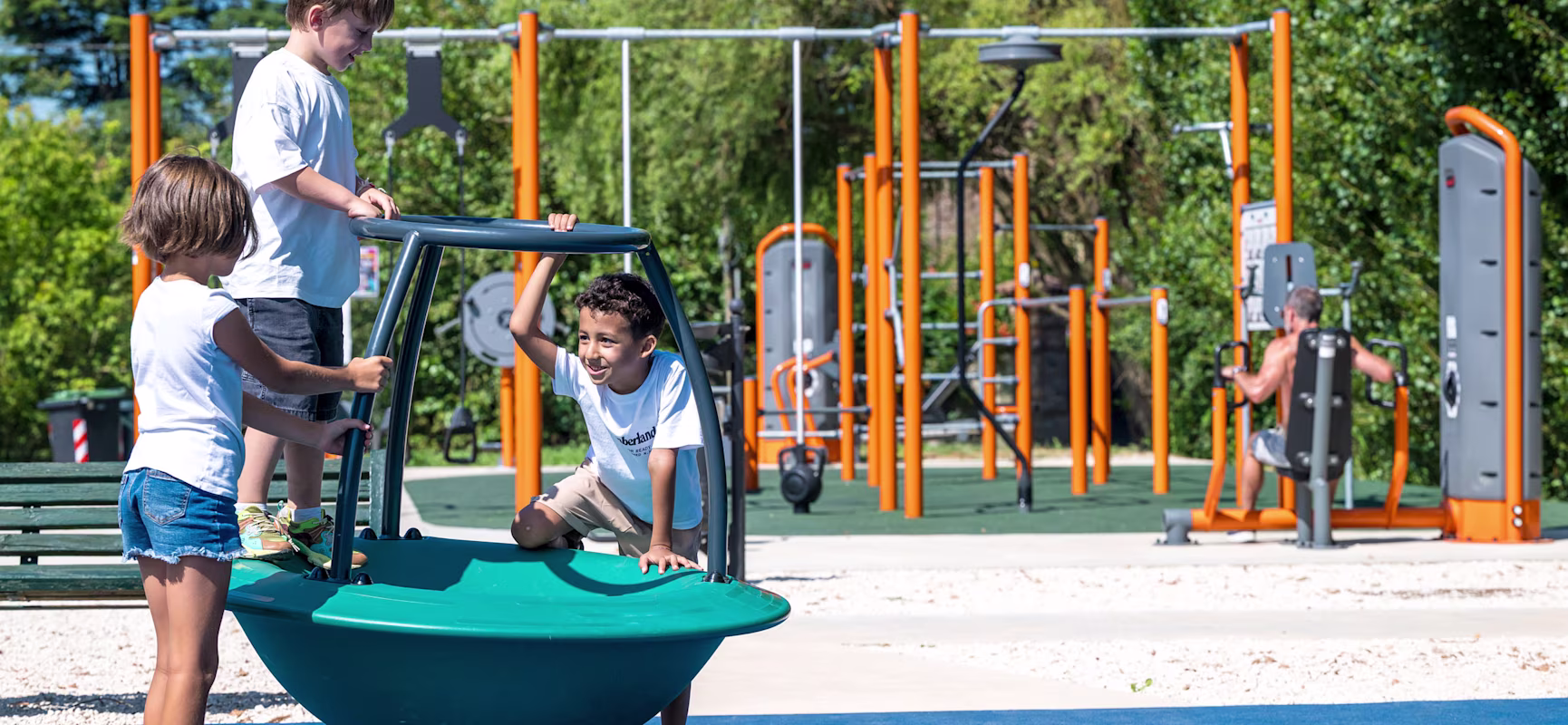 children playing on spinning playground equipment while man works out on outdoor gym