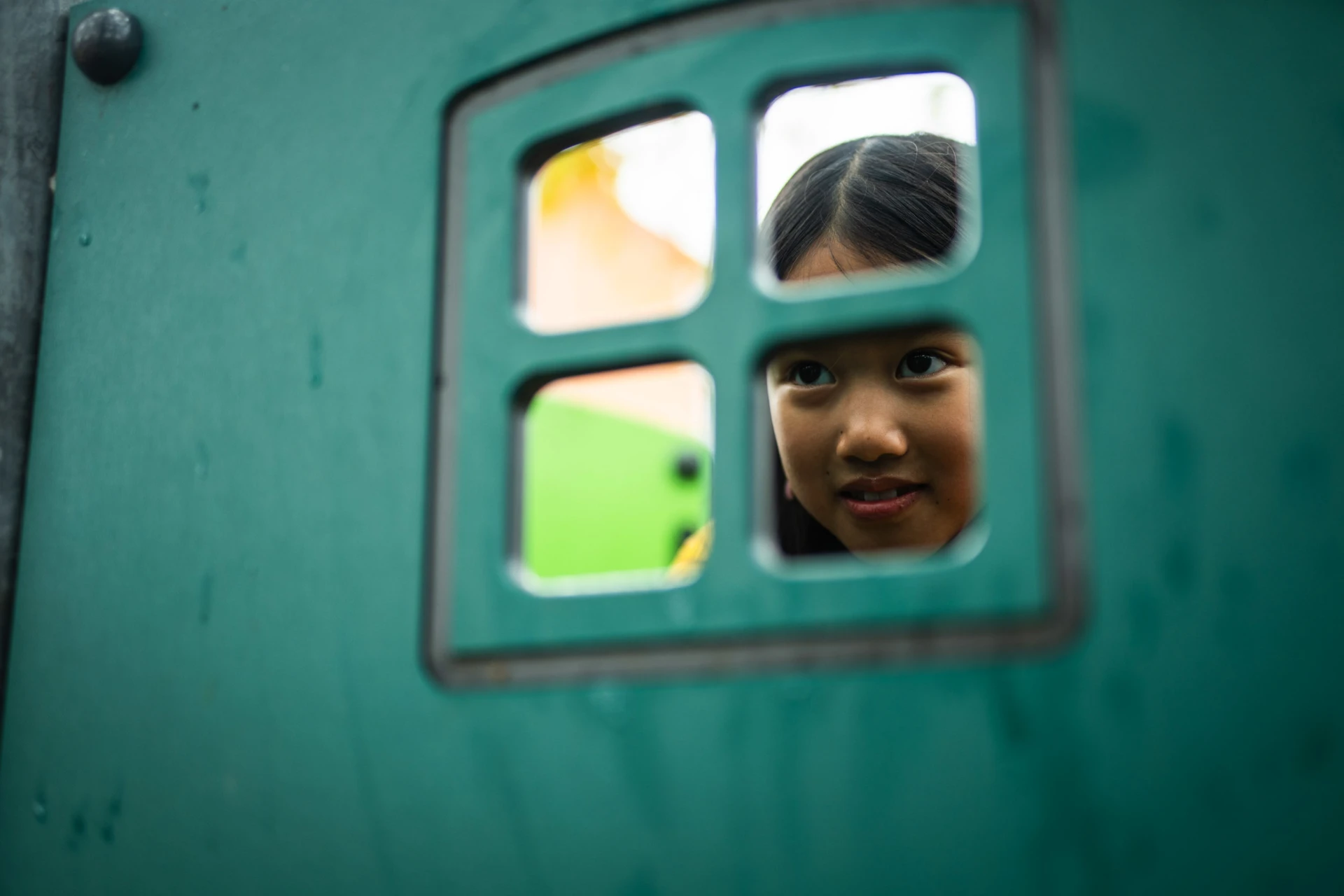 girl looking out of a window in a green playground panel