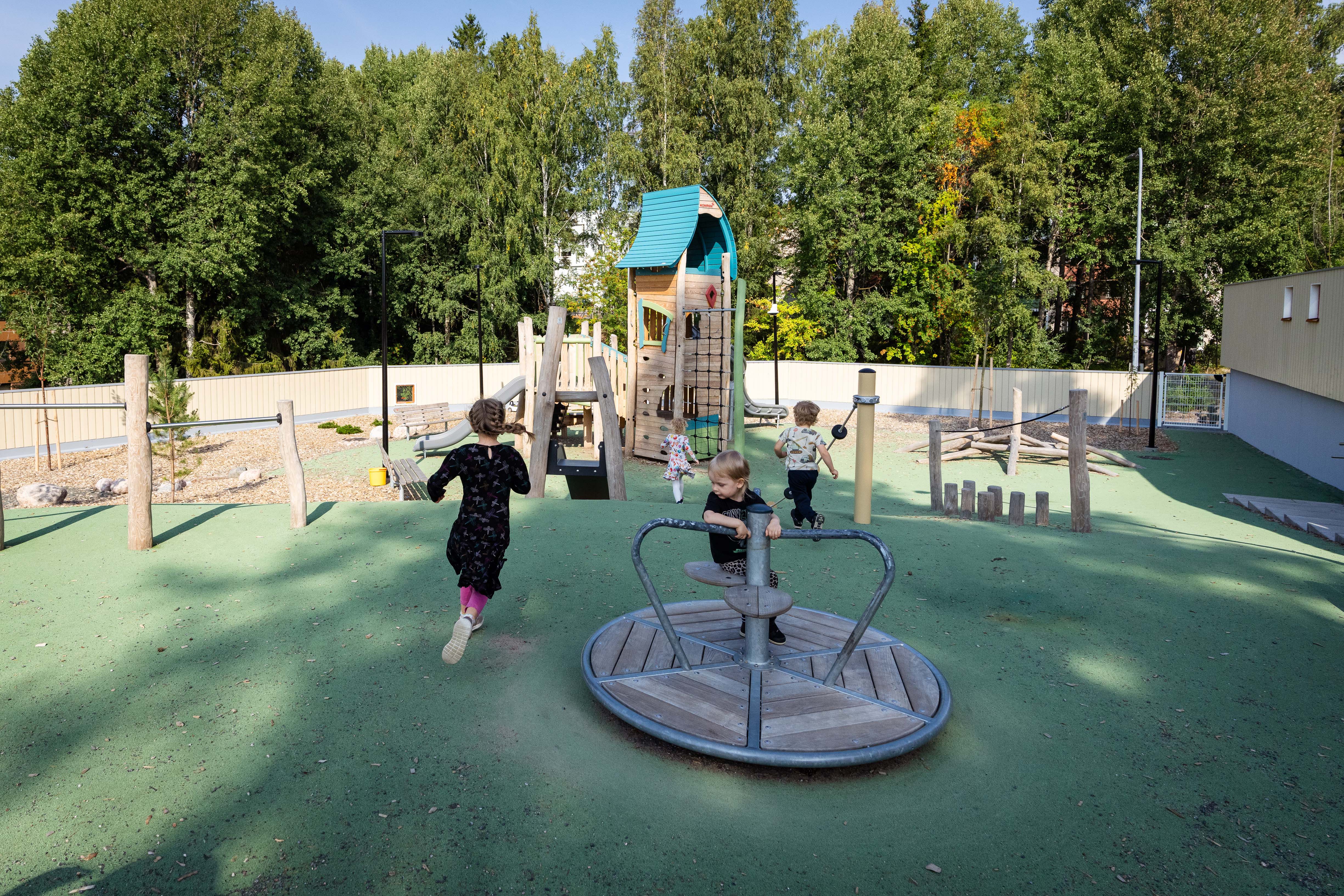 lapset juoksevat päiväkodin pihassa leikkivälineen luokse, yksi lapsi pyörii karusellissa