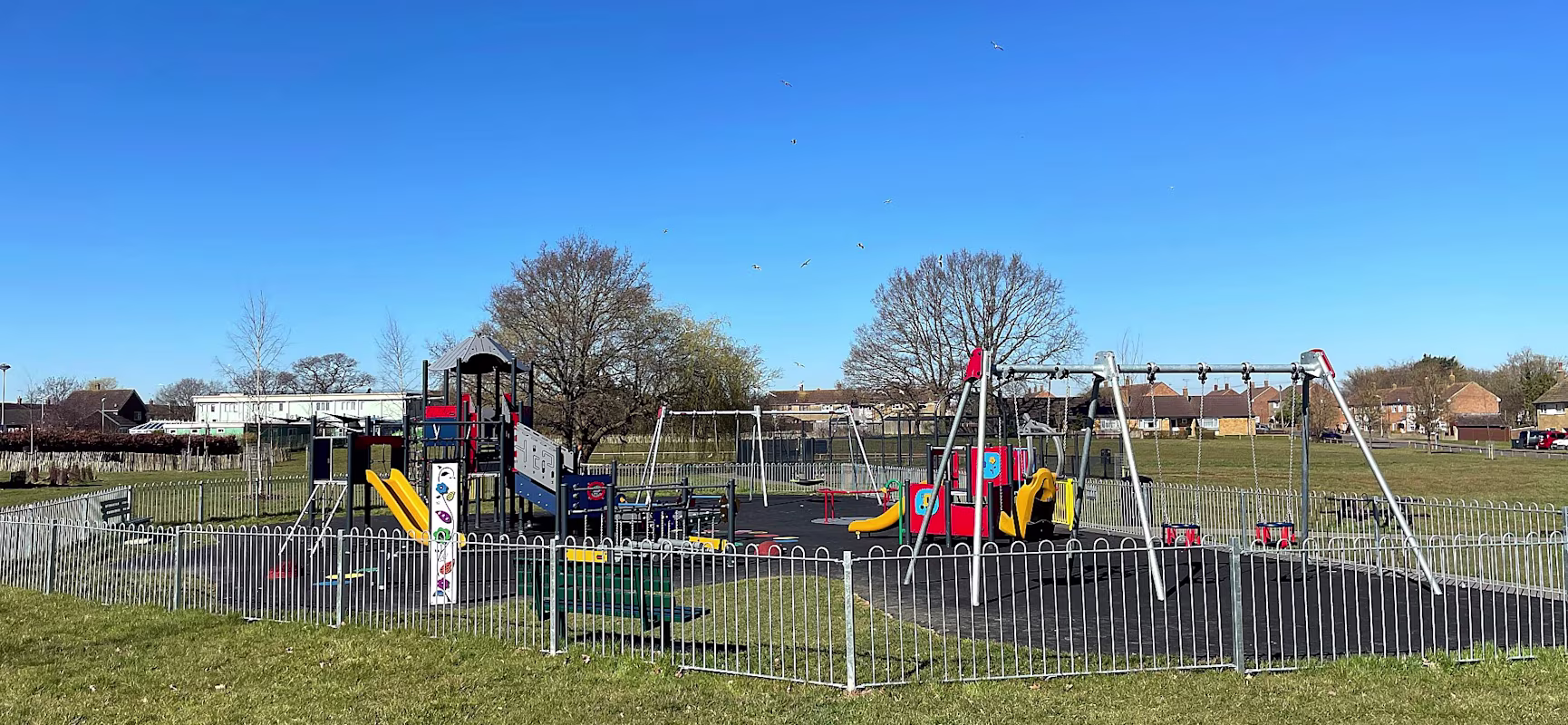 Fenced childrens playground with wings and colourful climbing unit with slides