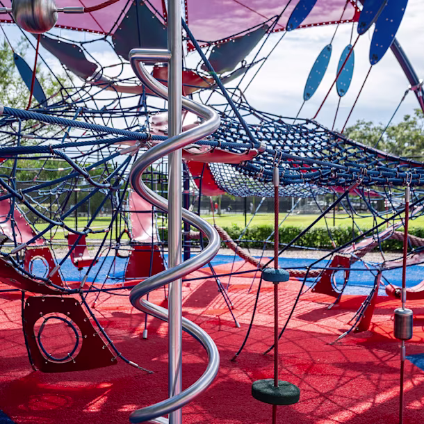 Close up shot of elements inside a shaded KOMPAN climbing dome, featuring a red and blue color palette