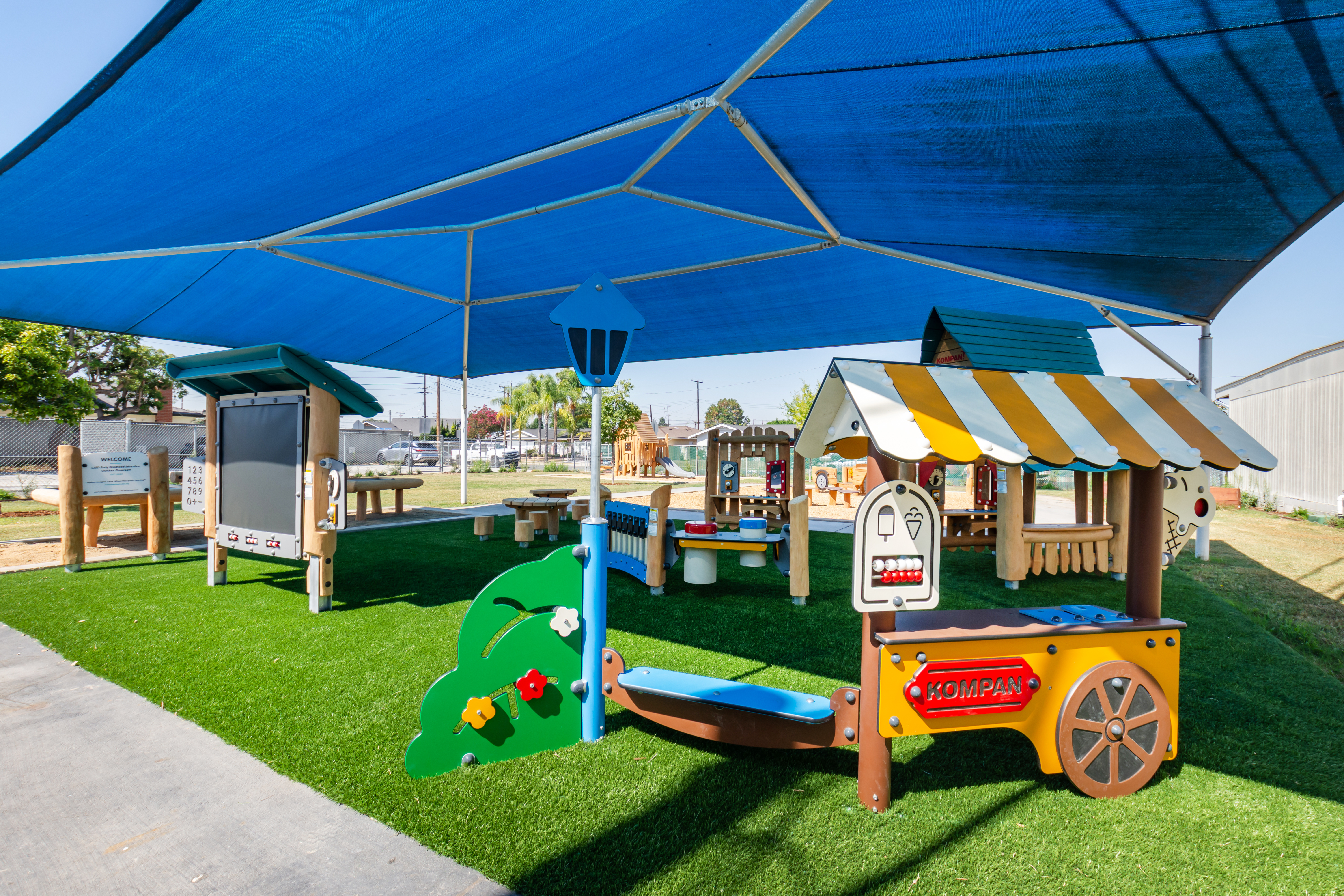 Shaded commercial playground equipment, featuring themed equipment, a blackboard, musical play panel, and more, at Maybrook Elementary in Whittier, California
