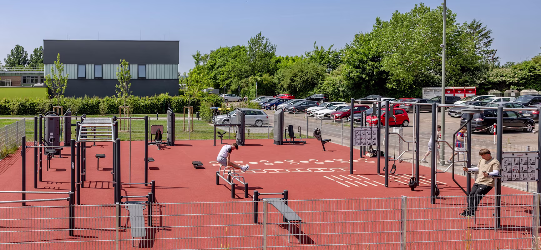 Zwei Frauen und ein Mann im Rollstuhl sitzen gemeinsam vor einem KOMPAN Fitnessplatz