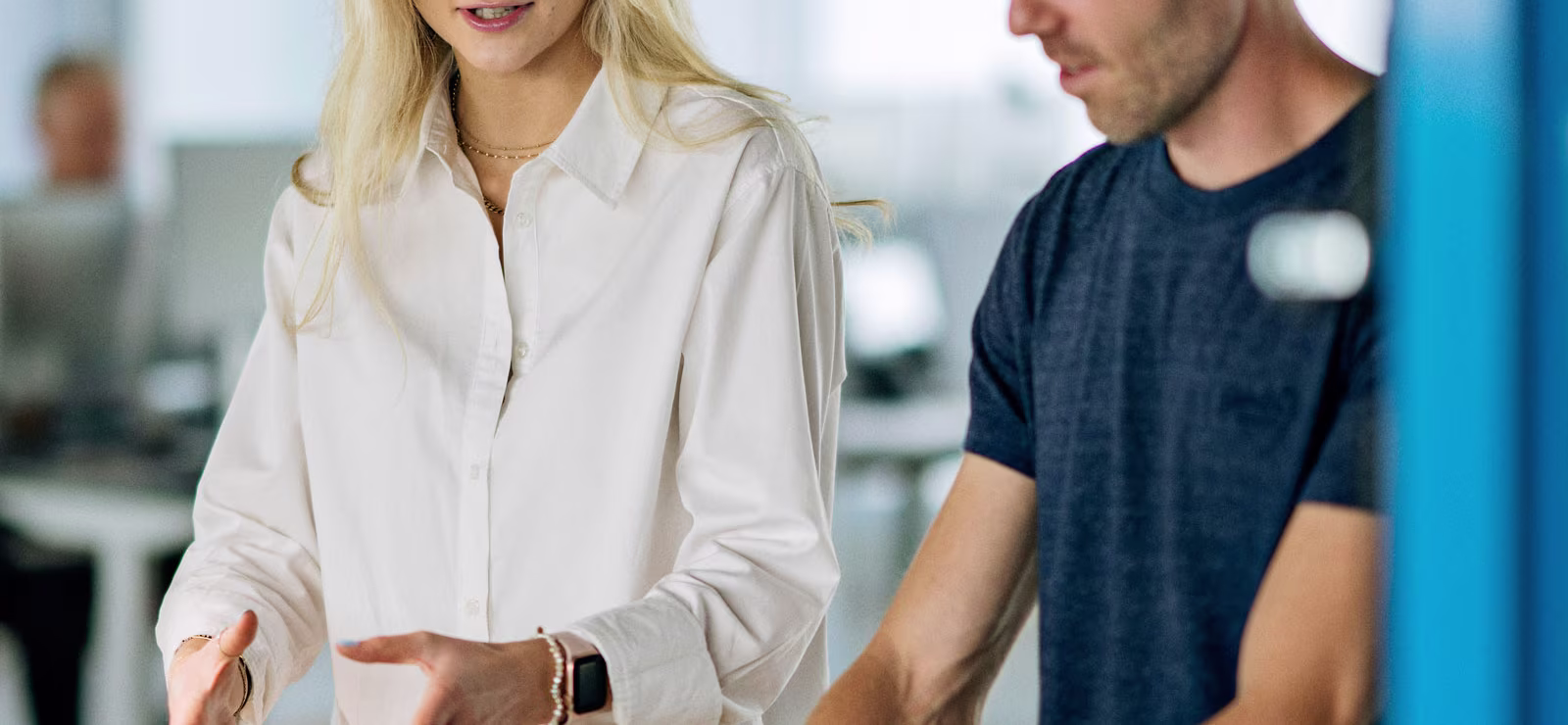 Two coworkers stand at a workbench arranging small wooden pieces on a green mat in a bright, modern office.