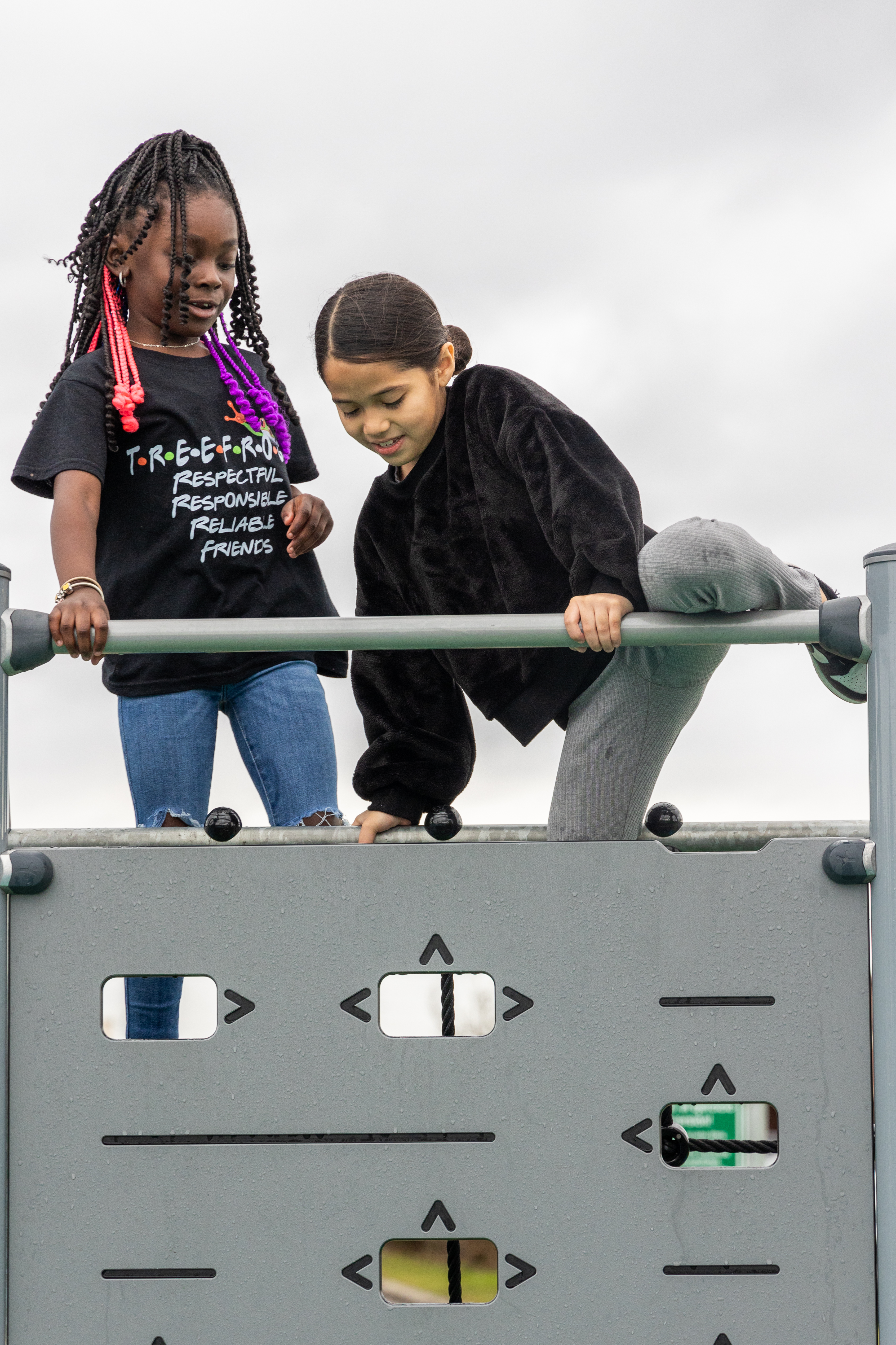 Two girls high-fiving each other sitting on a play structure
