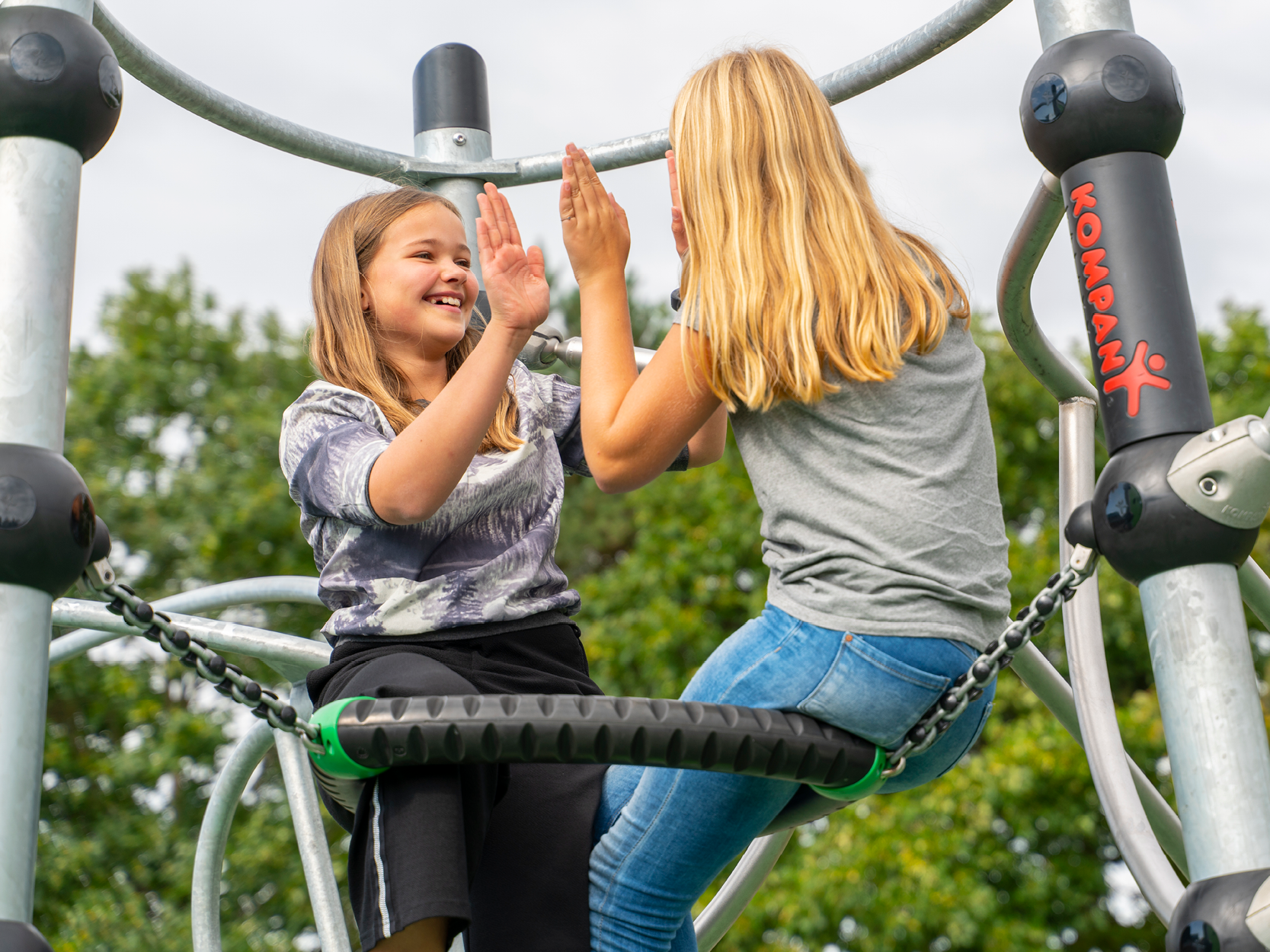 Two girls high-fiving each other sitting on a play structure