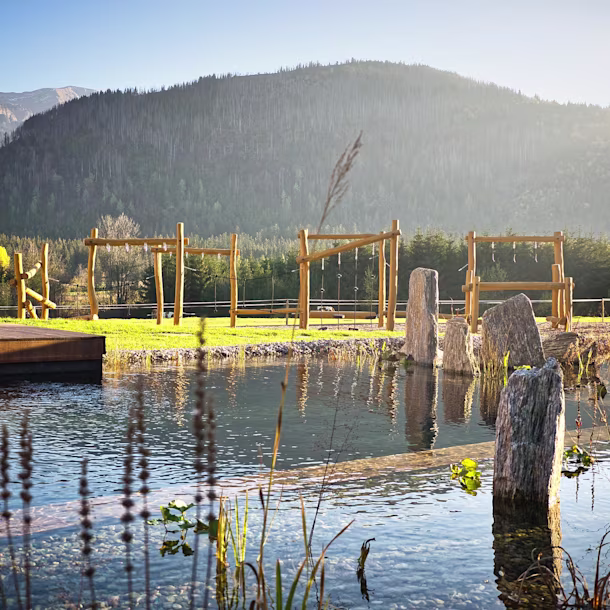 A pond with wooden playground and a mountain in the background.