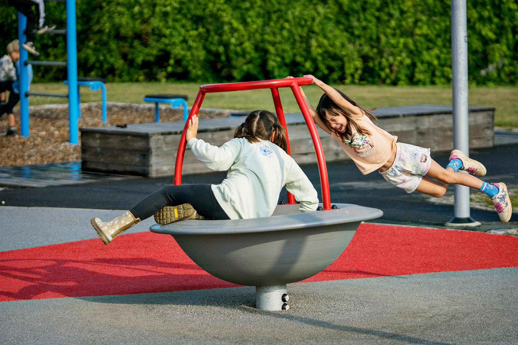 Girl sitting on a spinner while another girl hangs on it