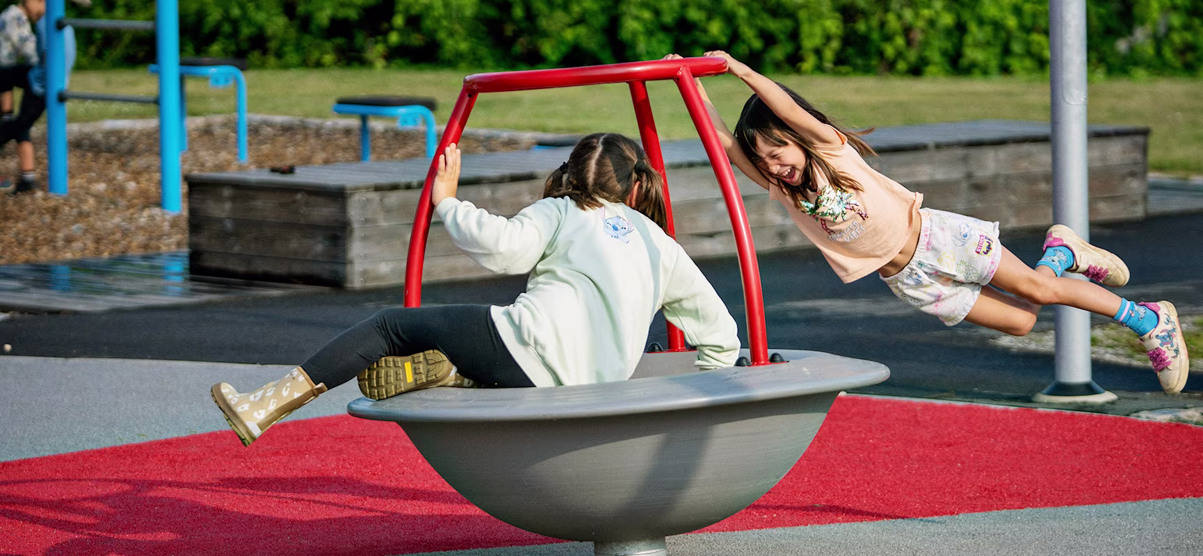 Girl sitting on a spinner while another girl hangs on it