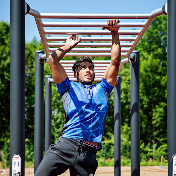 Person in blue sports shirt swinging on outdoor monkey bars at a park under a clear blue sky.