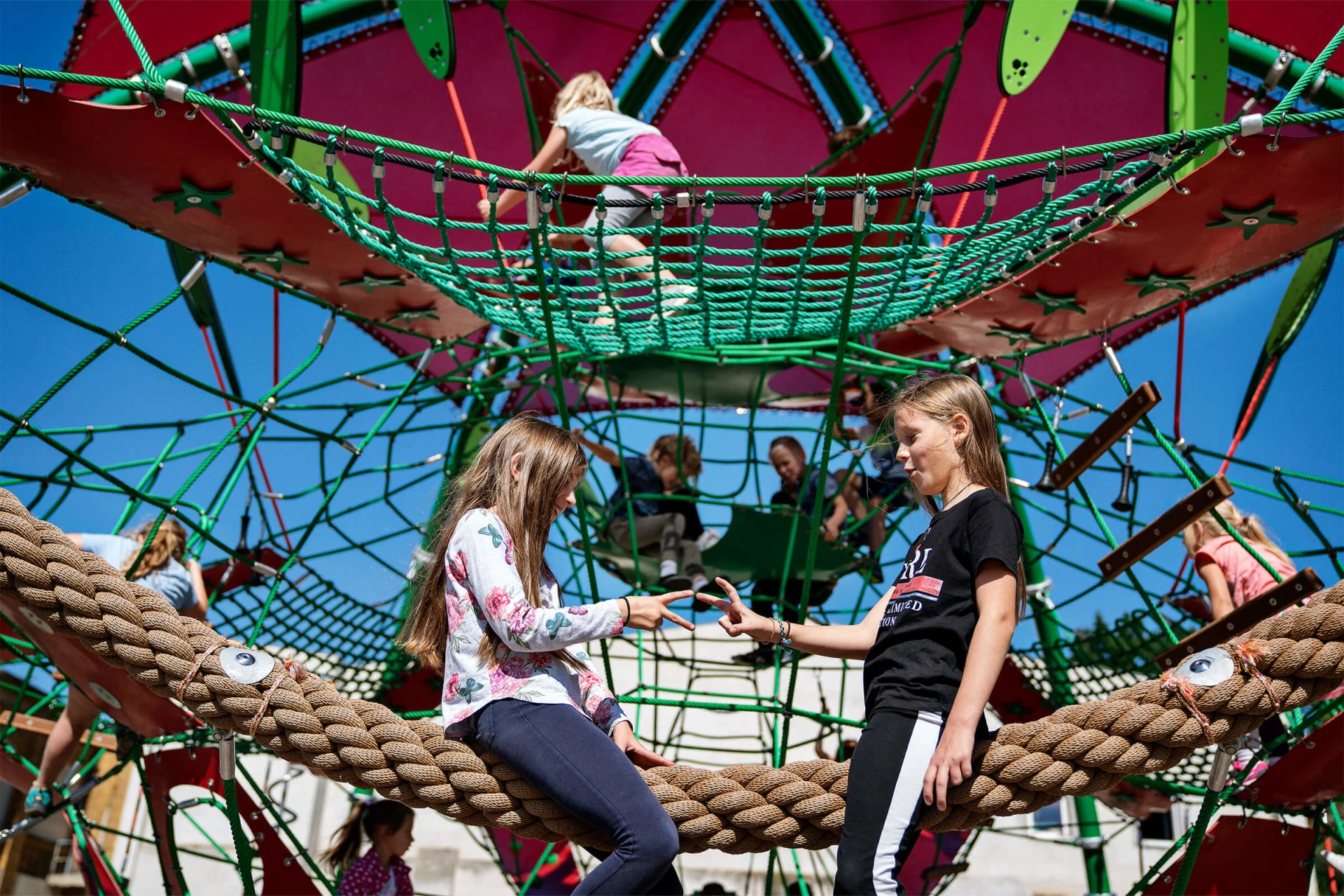 Zwei Mädchen sitzend auf einem Seilkletterspielplatz