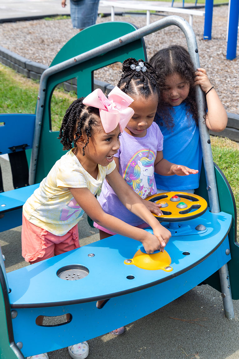 Three preschool-age children playing in a car-themed piece of early years outdoor play equipment.