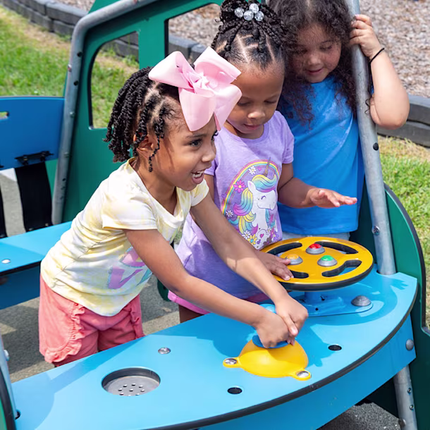 Three preschool-age children playing in a car-themed piece of early years outdoor play equipment.