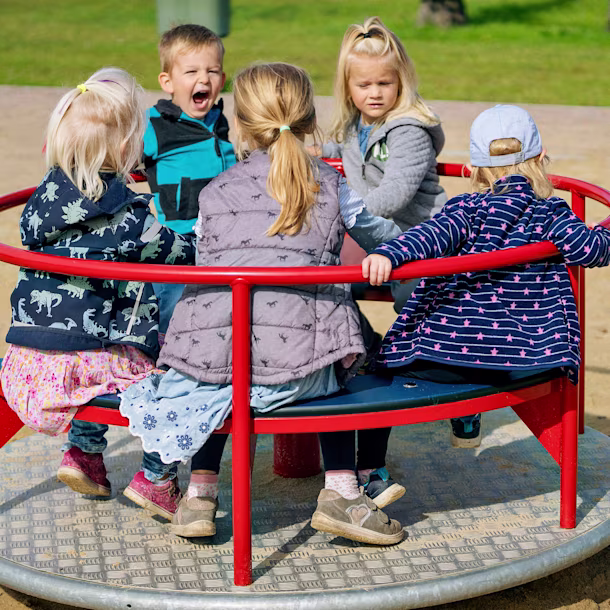 Kitakinder spielen auf einem Spielplatzkarussell in Ihlow, Deutschland