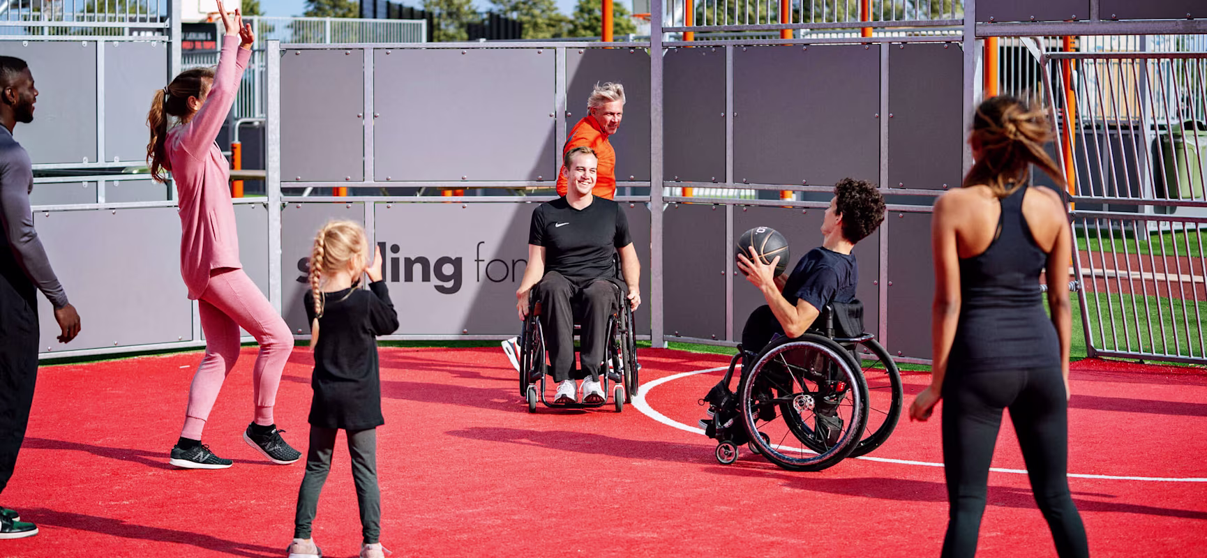 Människor i rullstol och utan rullstol spelar basket på multiarena med gummiasfalt