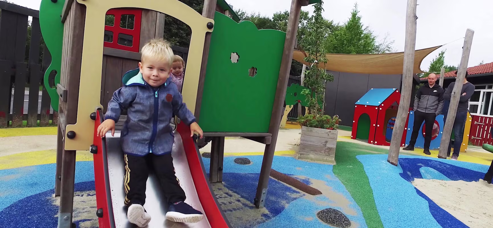 Child in kindergarten sliding down a slide on toddler equipment