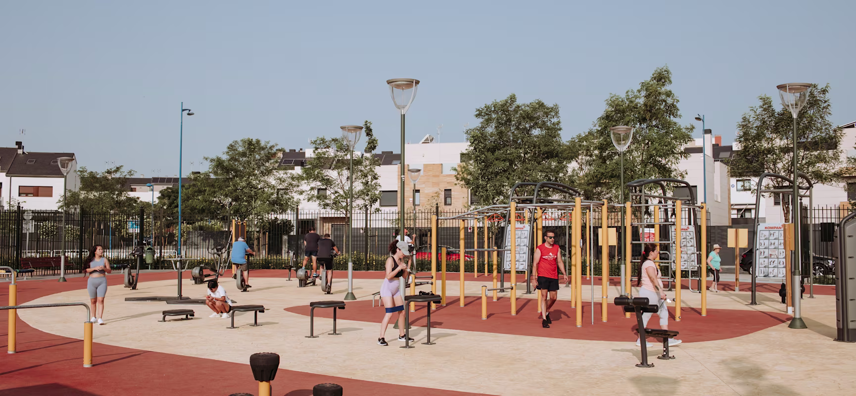 Red fish-shaped climbing playground with nets and slide in a sunny park, surrounded by green trees and nearby apartment buildings.