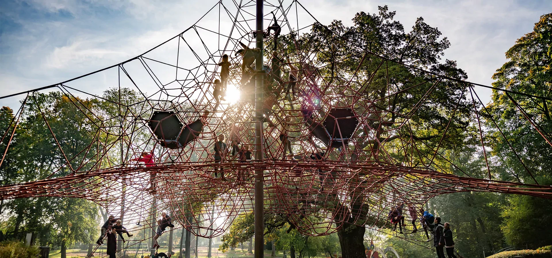 many children climbing a large pyramid rope climbing net playground hero image