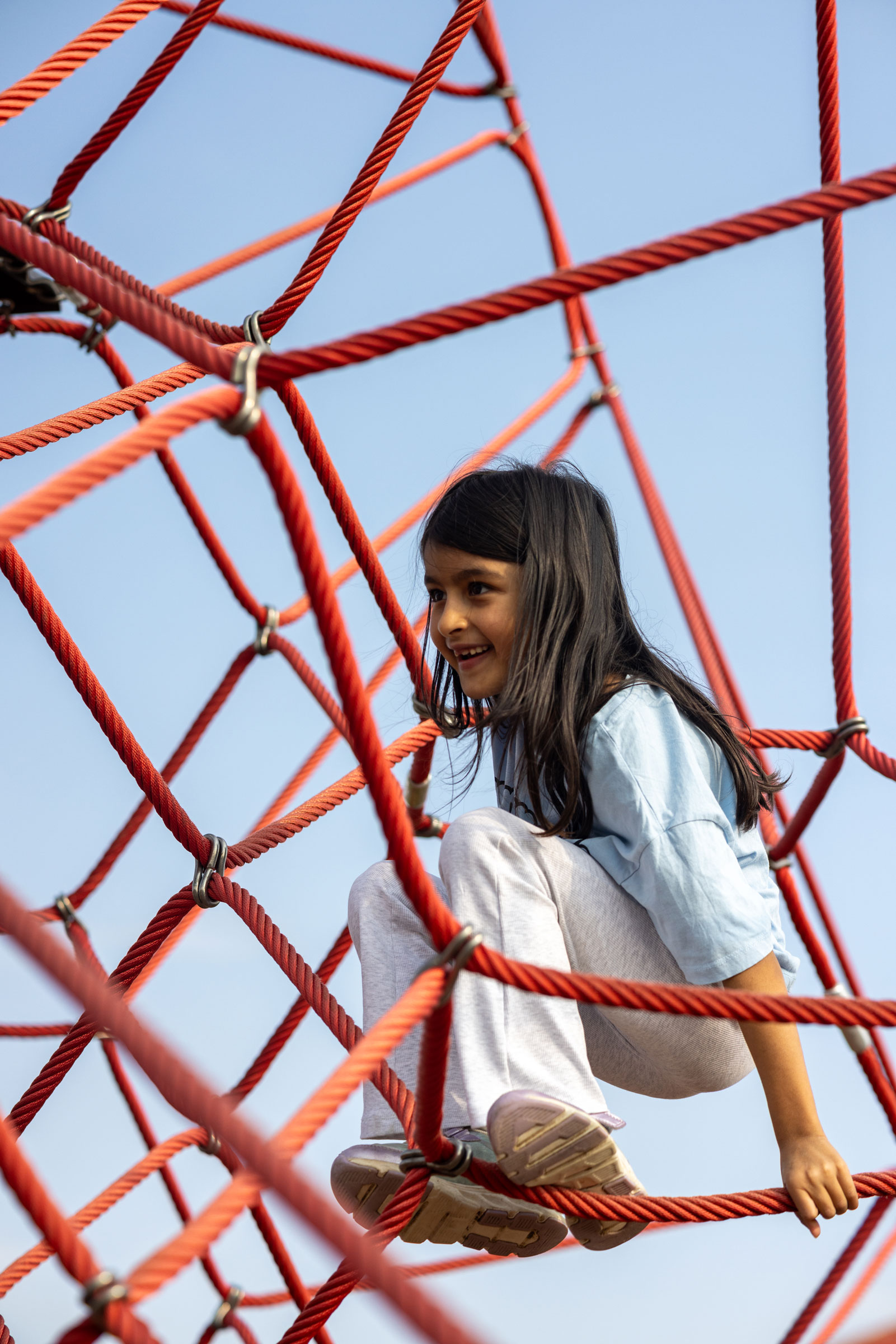 many children climbing a large pyramid rope climbing net playground hero image