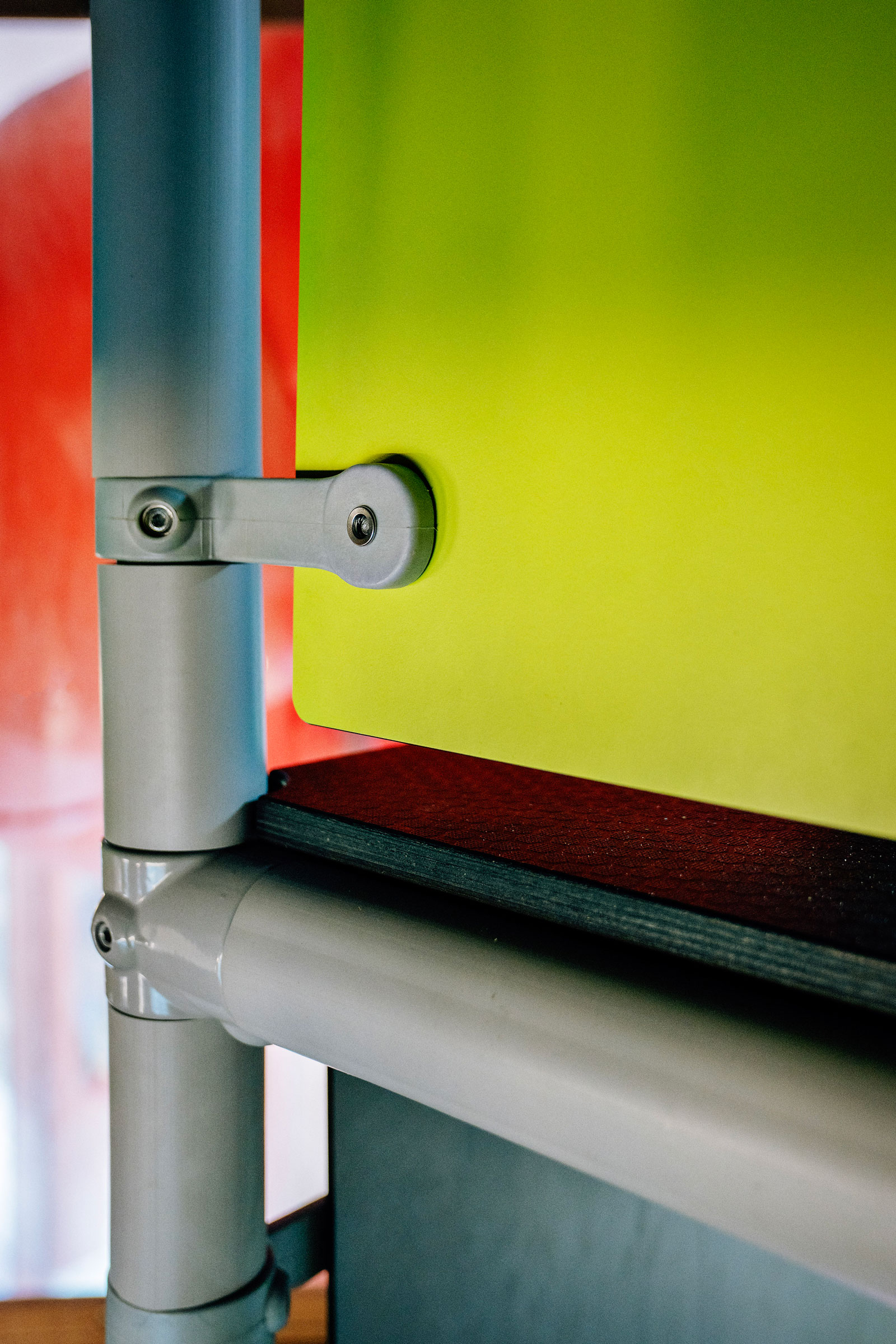 Close-up of grey metal pipes and brackets supporting a bright yellow panel, with red and dark surfaces in the background.