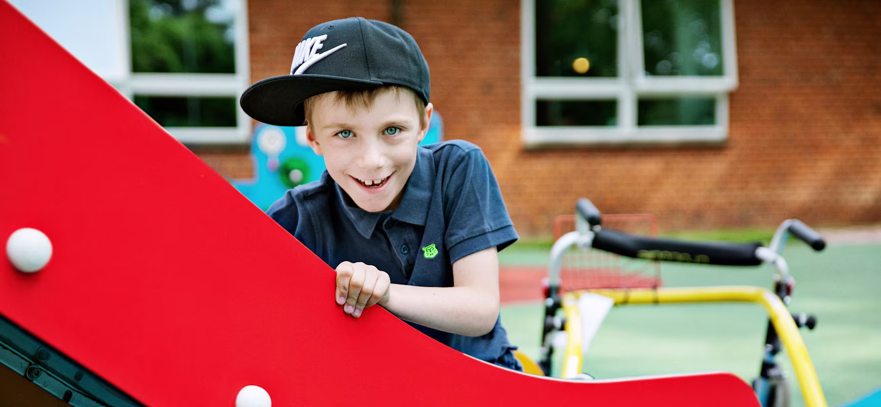 Boy with a walker sitting on a slide on inclusive play system