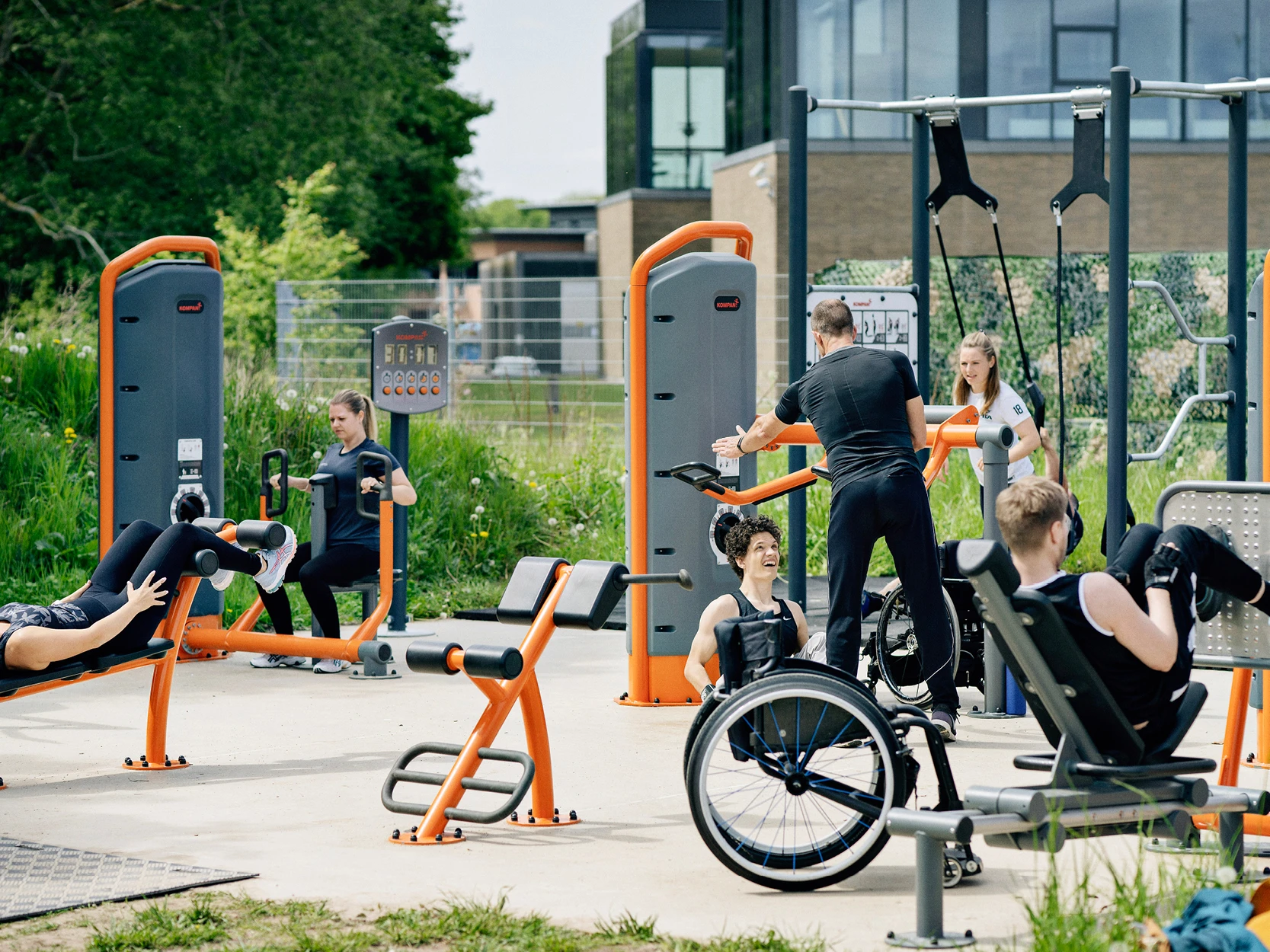 En grupp människor med och utan rullstolar som använder utegymutrustning i en park