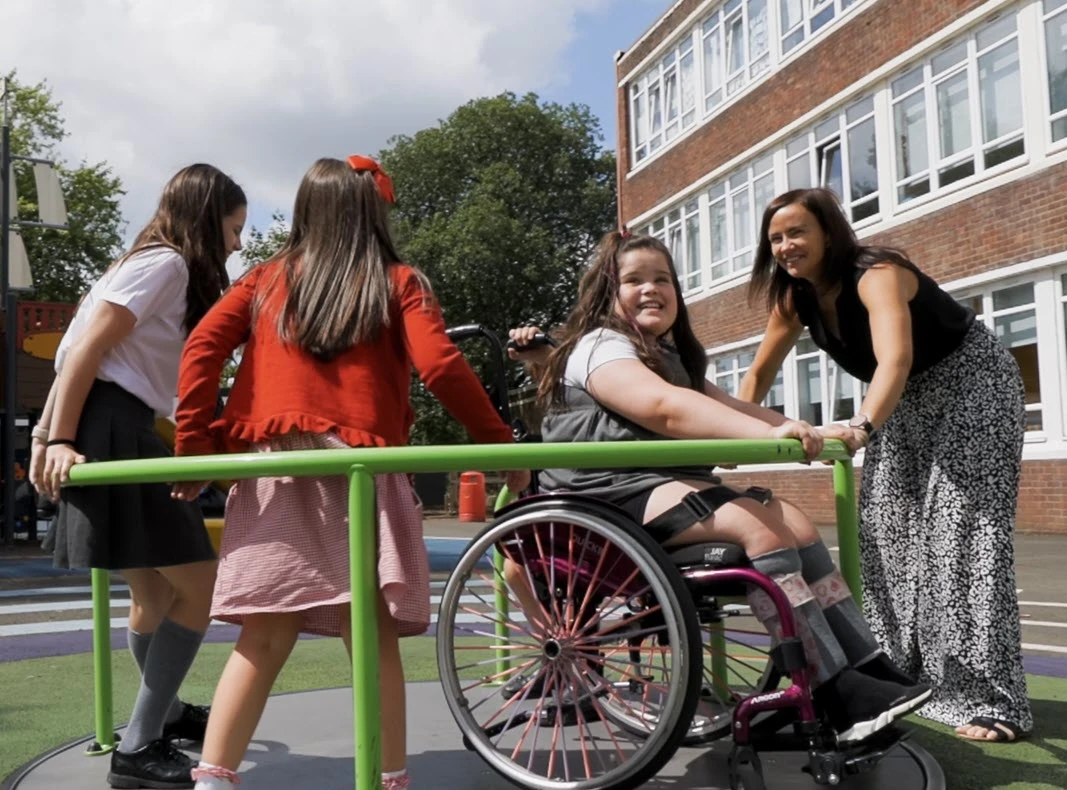 en flicka i rullstol åker karusell med andra barn på inkluderande skolgård