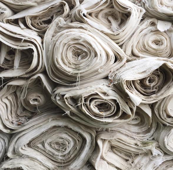 Close-up of tightly rolled, off-white fabric bundles stacked together, showing frayed edges and layered textile textures.
