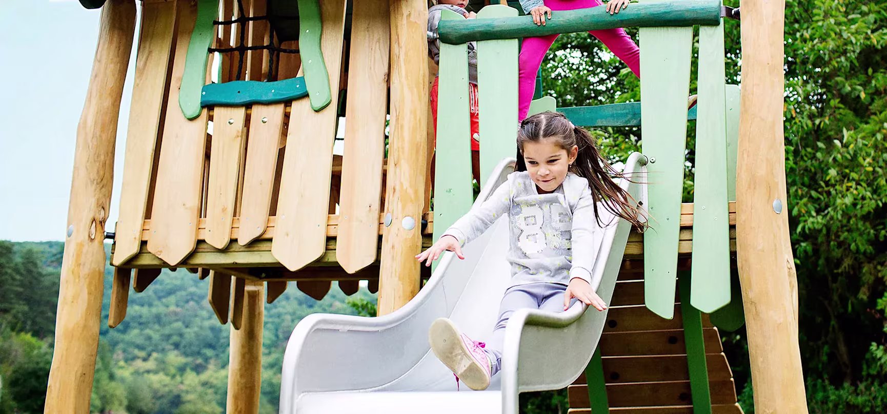 child sliding on a wooden playground set slide robnia play systems hero image