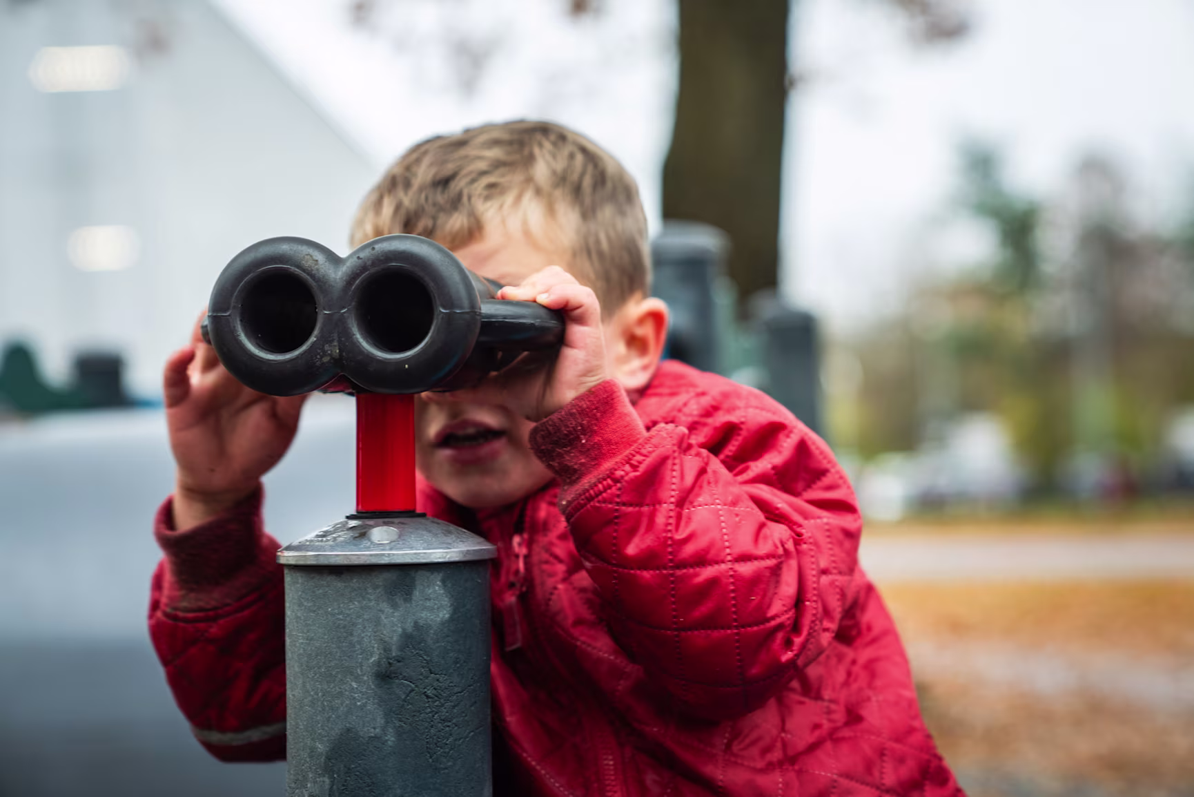 boy in red clothes looking through binoculars on a playground