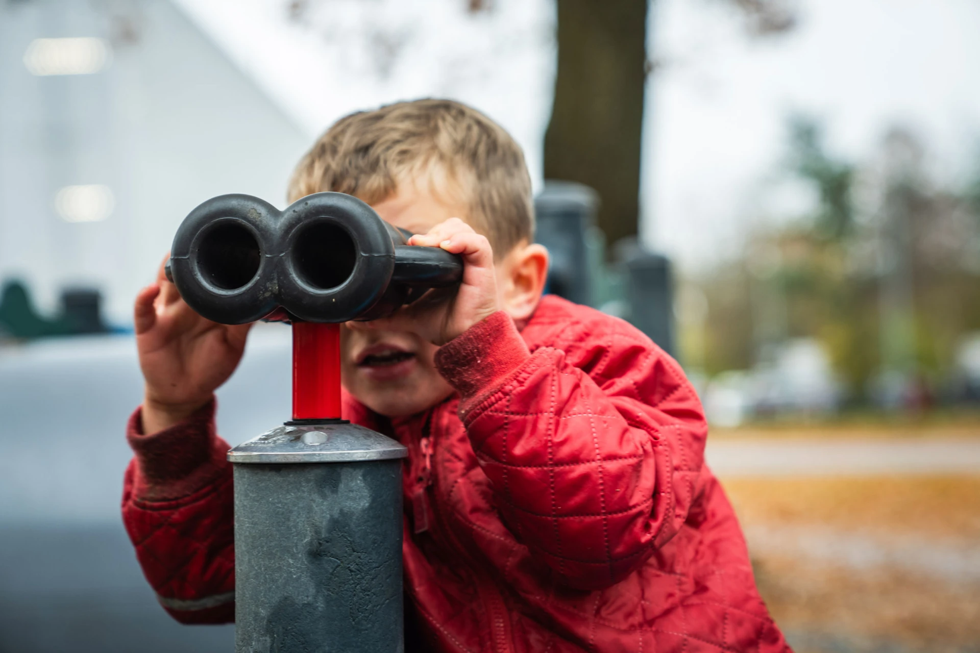 niño vestido de rojo mirando con prismáticos en un parque infantil