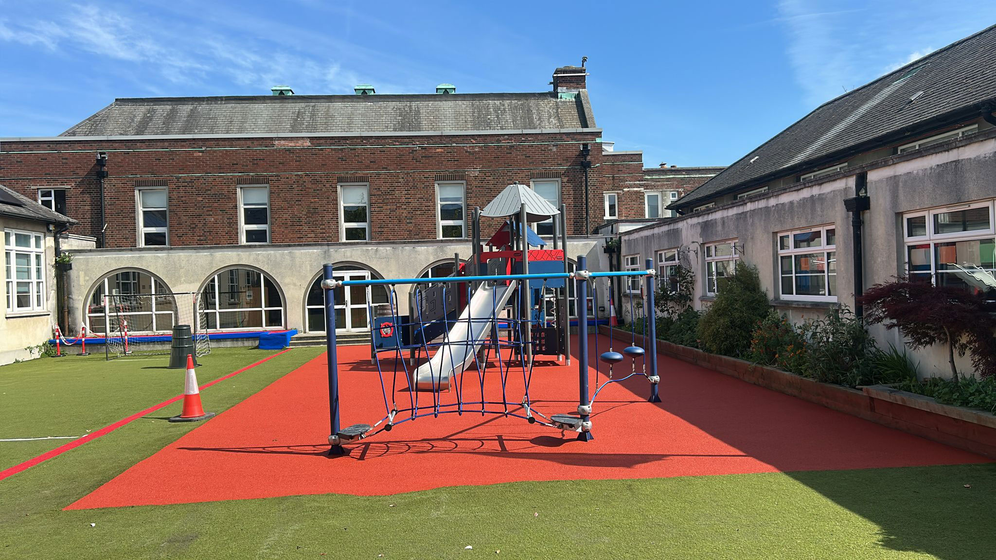 Children climb and play on a tall rope structure in a sunny playground with slides and sand underneath