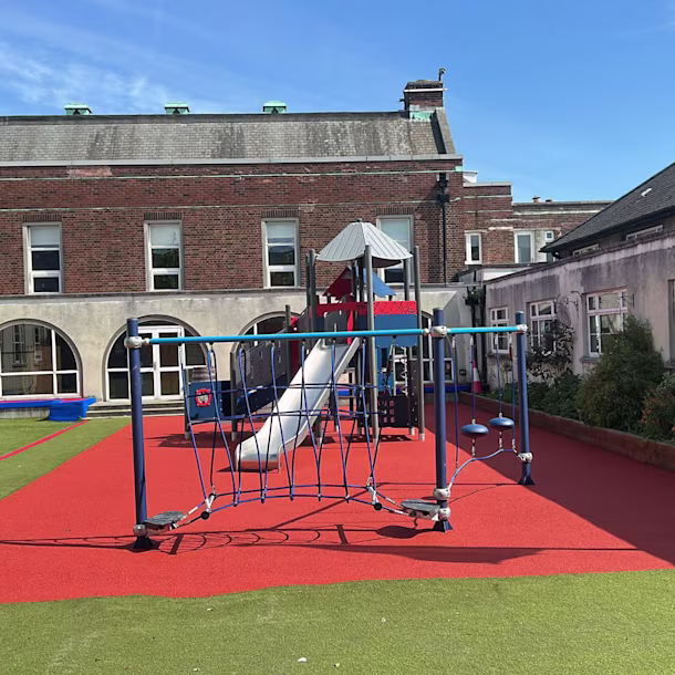 Children climb and play on a tall rope structure in a sunny playground with slides and sand underneath