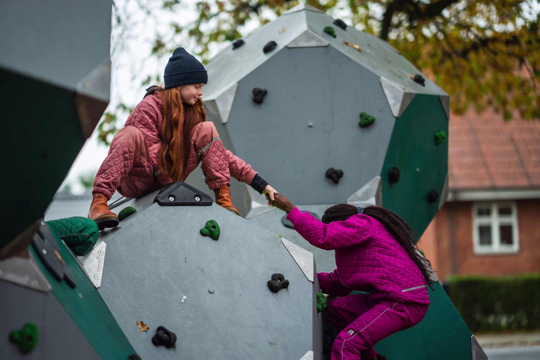 A girl helping another girl climbing up on a climbing structure on a playground