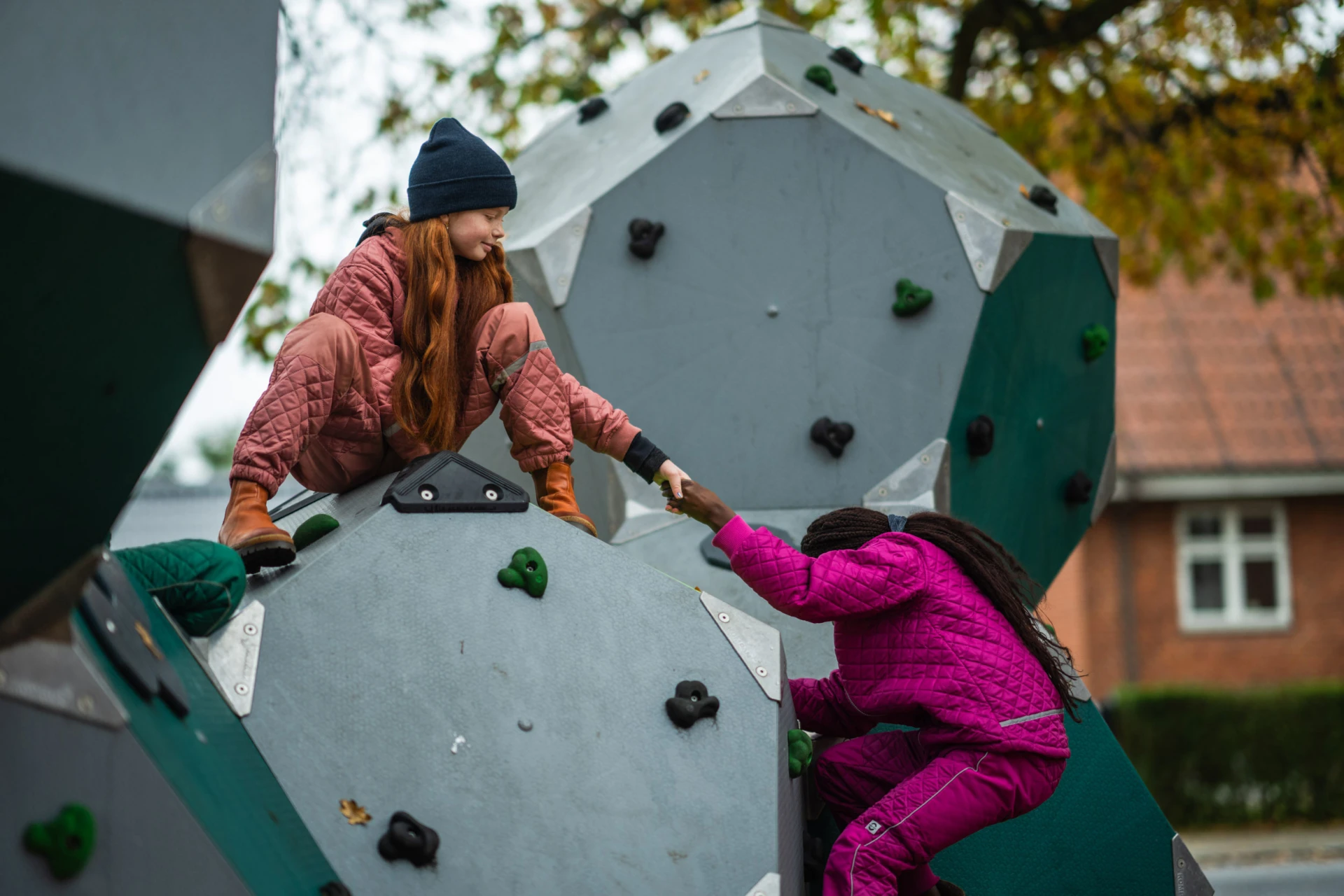 Una ragazza che aiuta un'altra ragazza ad arrampicarsi su una struttura di arrampicata in un parco giochi
