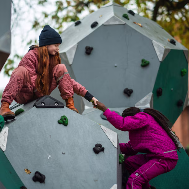 Une fille aide une autre fille à grimper sur une structure d'escalade dans une aire de jeux.