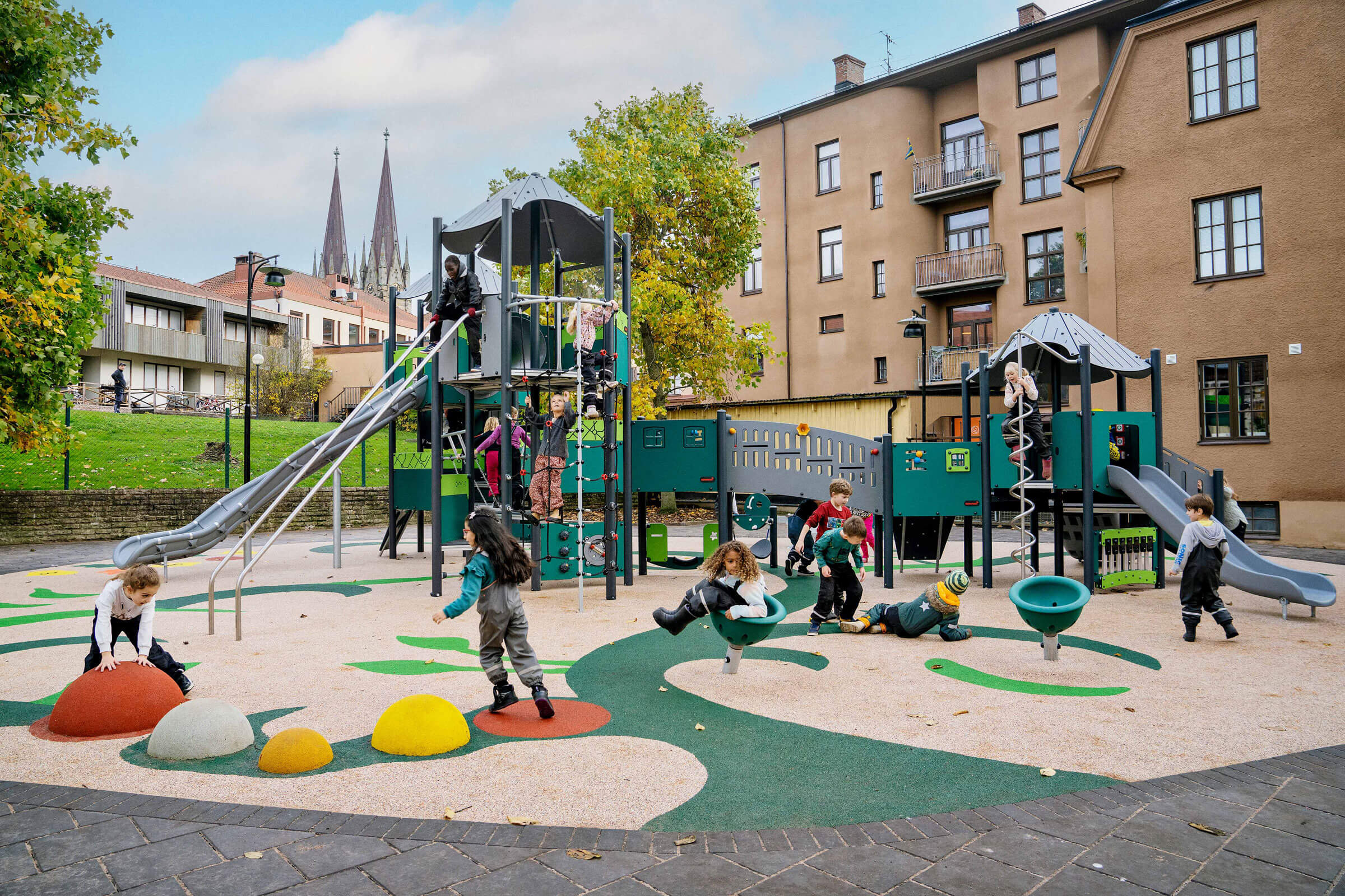 Viele Kinder spielen fröhlich auf einem Spielplatz mit Klettergerüst und freistehenden Spielgeräten