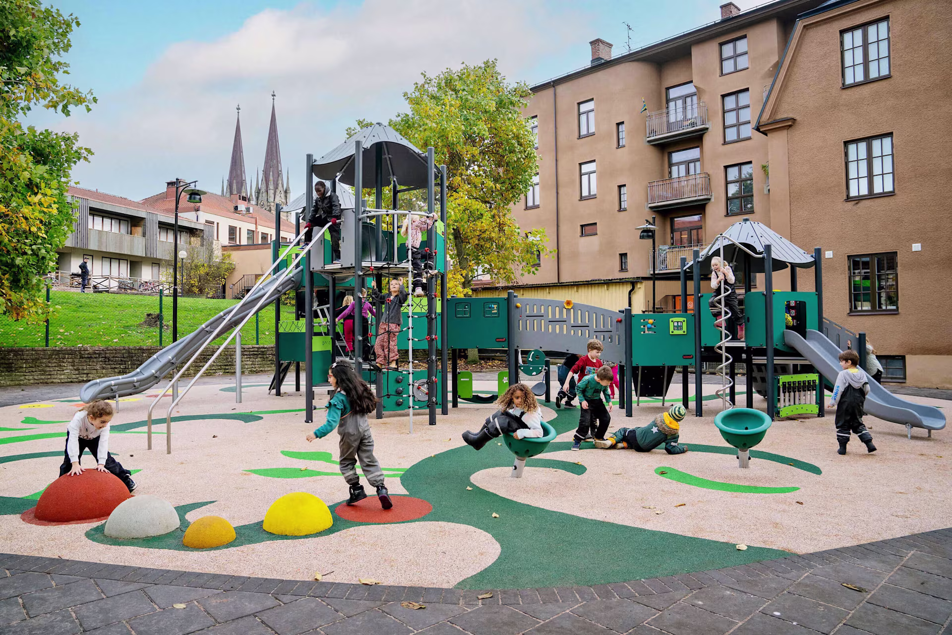 Viele Kinder spielen fröhlich auf einem Spielplatz mit Klettergerüst und freistehenden Spielgeräten