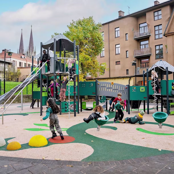 Viele Kinder spielen fröhlich auf einem Spielplatz mit Klettergerüst und freistehenden Spielgeräten